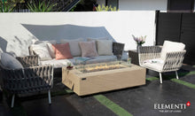 Load image into Gallery viewer, Elementi Plus Colorado Fire Table with flame and wind guard in a patio setting