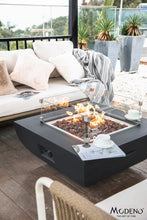 Load image into Gallery viewer, Modeno by Elementi Aurora fire pit table shown with a flame  and wind guardon a patio