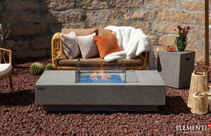 elementi plus monte carlo fire pit table on a beautiful patio with wind guard and flame.