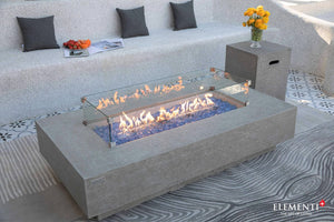 elementi plus riviera fire table in grey with flame , tank cover and wind guard on a patio