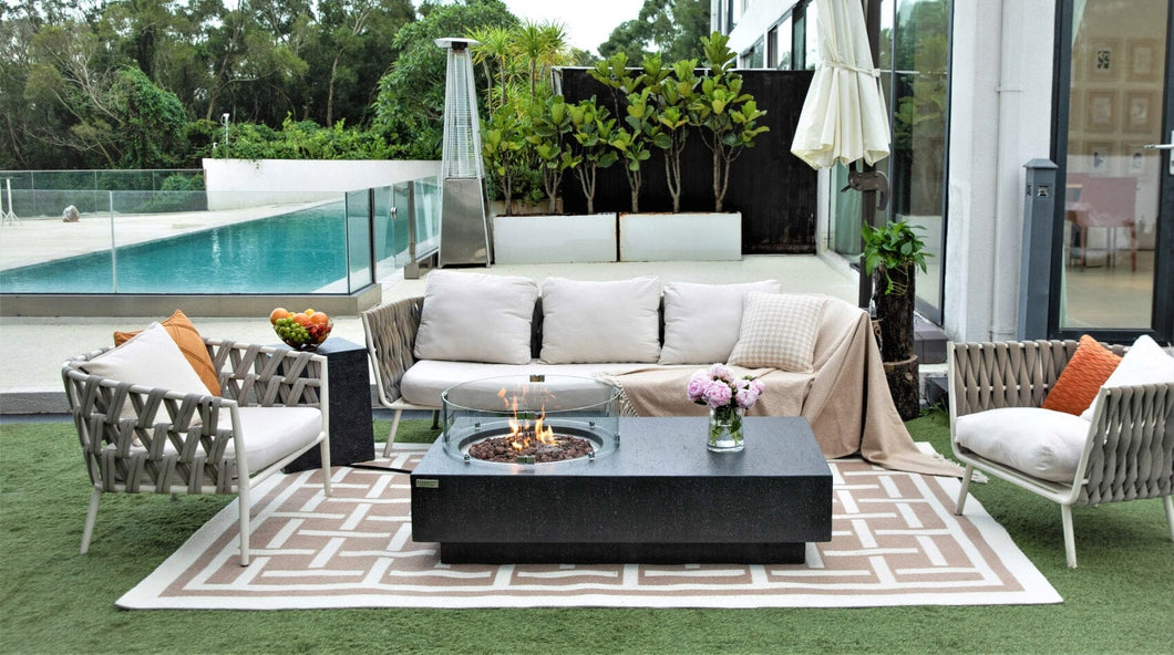 Elementi metropolis fire table in dark gray. Shown on a patio with flame and wind guard